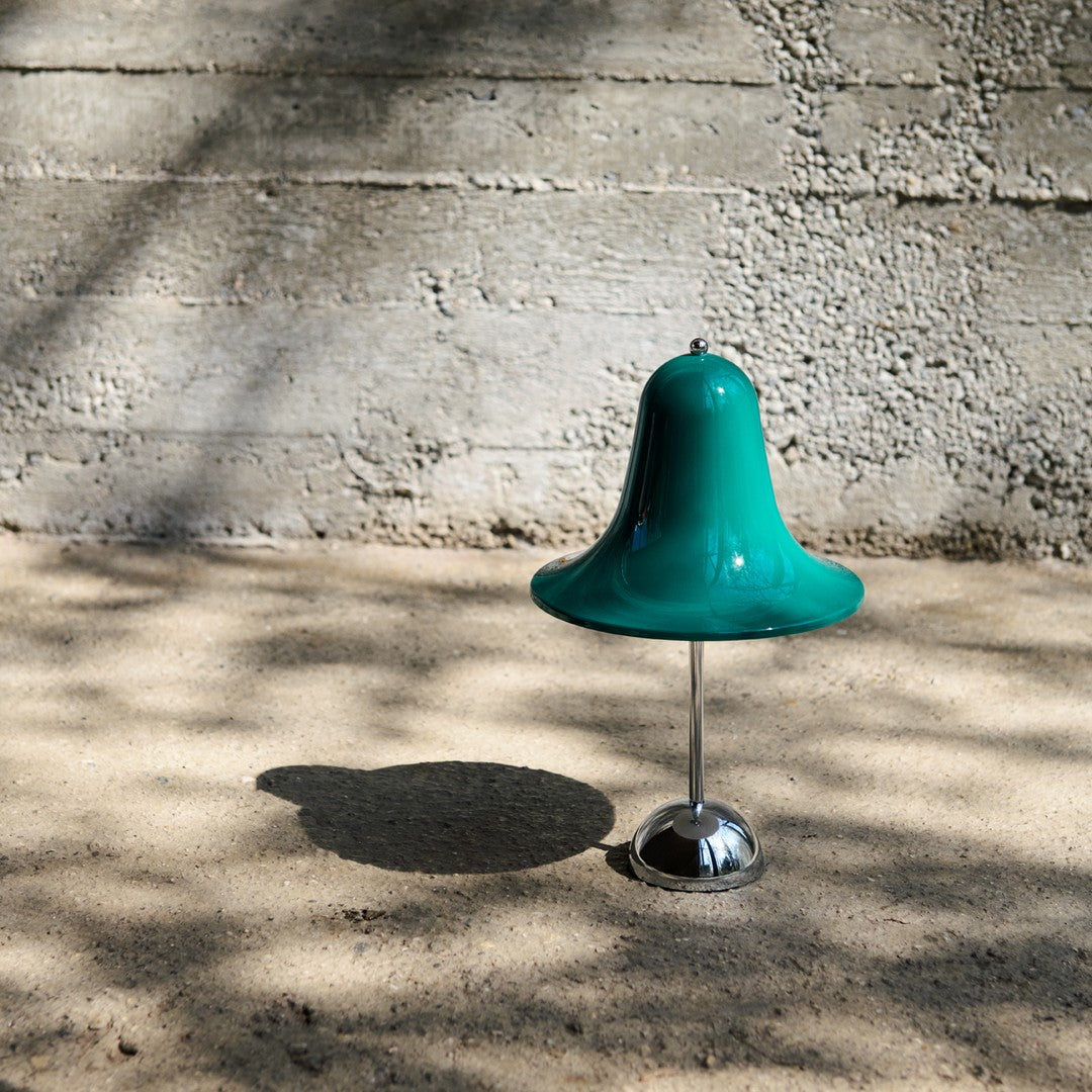 Teal bell-shaped decor on a silver stand, with soft shadows and a textured gray background.
