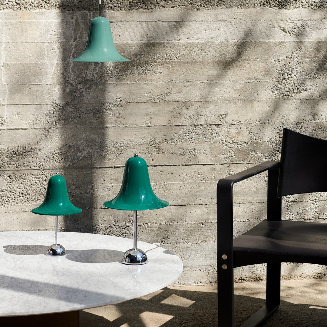 Green bell-shaped pendant and table lamps with chrome bases, contrasted against a textured gray wall and wooden furniture.