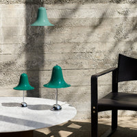 Green bell-shaped pendant and table lamps with chrome bases, contrasted against a textured gray wall and wooden furniture.