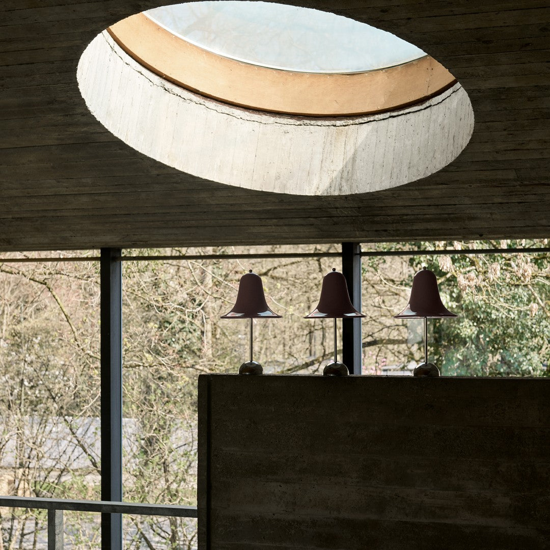 Modern pendant lamps in muted maroon with a round, soft-lit skylight and neutral gray walls. Elegant, minimalist design.