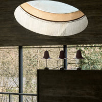 Modern pendant lamps in muted maroon with a round, soft-lit skylight and neutral gray walls. Elegant, minimalist design.
