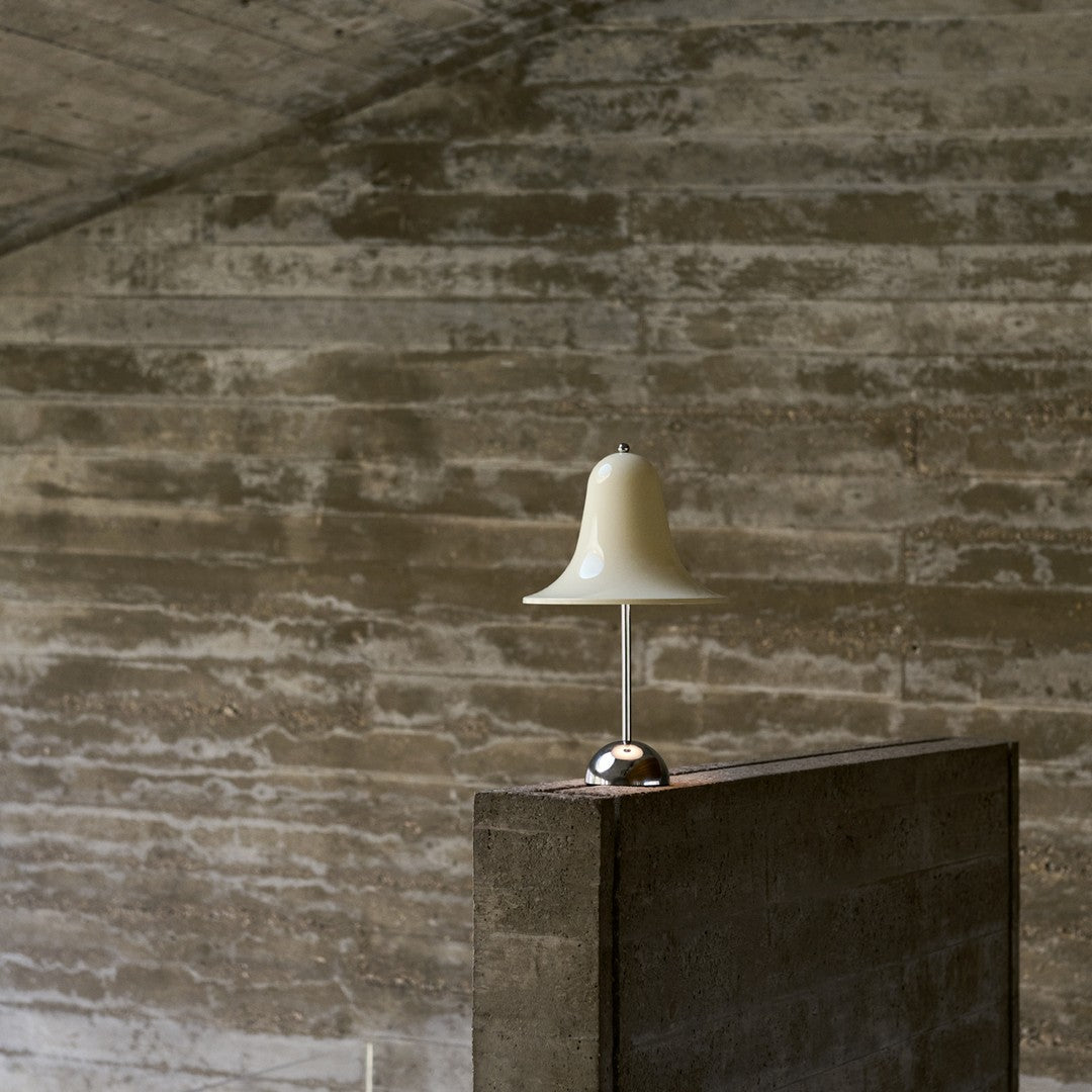 "Elegant white lamp with a bell-shaped shade atop a sleek gray concrete base, against a textured gray wall."