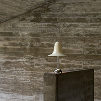 "Elegant white lamp with a bell-shaped shade atop a sleek gray concrete base, against a textured gray wall."
