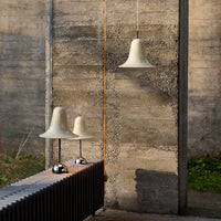 Cream bell-shaped lamps with chrome bases against a textured concrete backdrop, featuring green grass and natural tones.