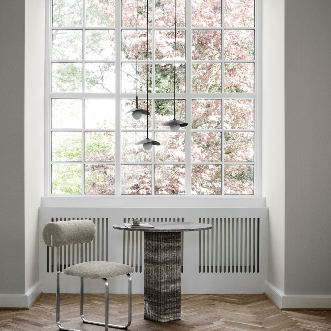 Elegant gray chair and textured stone table with soft hues, set against a backdrop of natural light and greenery.