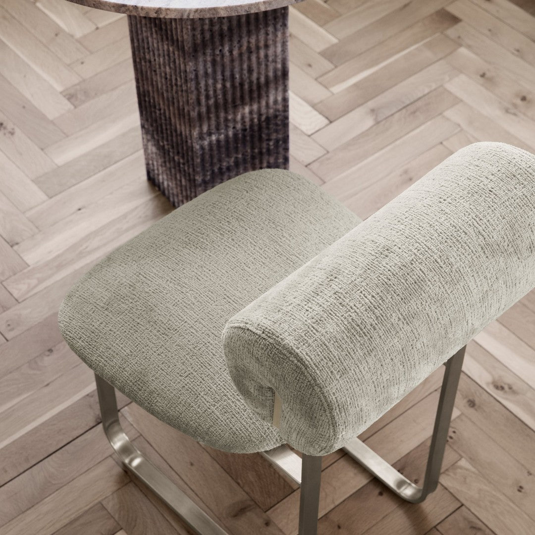 Soft grey upholstered chair with a textured pattern, set on a light wooden floor with a geometric accent table.