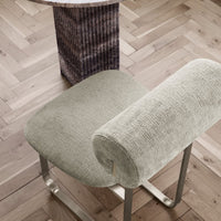 Soft grey upholstered chair with a textured pattern, set on a light wooden floor with a geometric accent table.