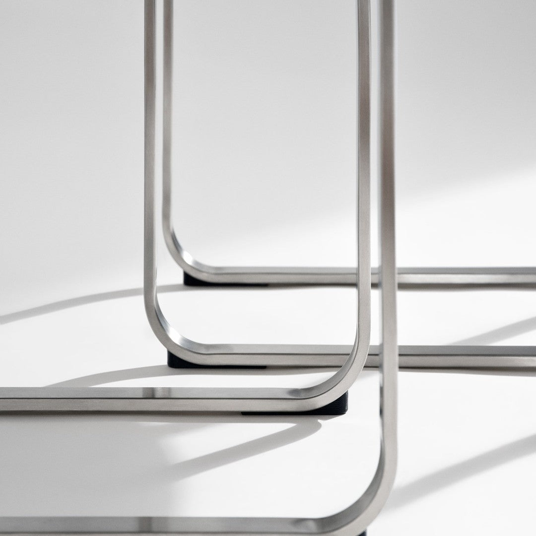 Stylish silver metal frame with sleek curved edges and contrasting black feet on a soft gray background.