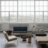 Modern furniture in muted tones: navy blue, natural beige, and metallic bronze accents on a light concrete floor.
