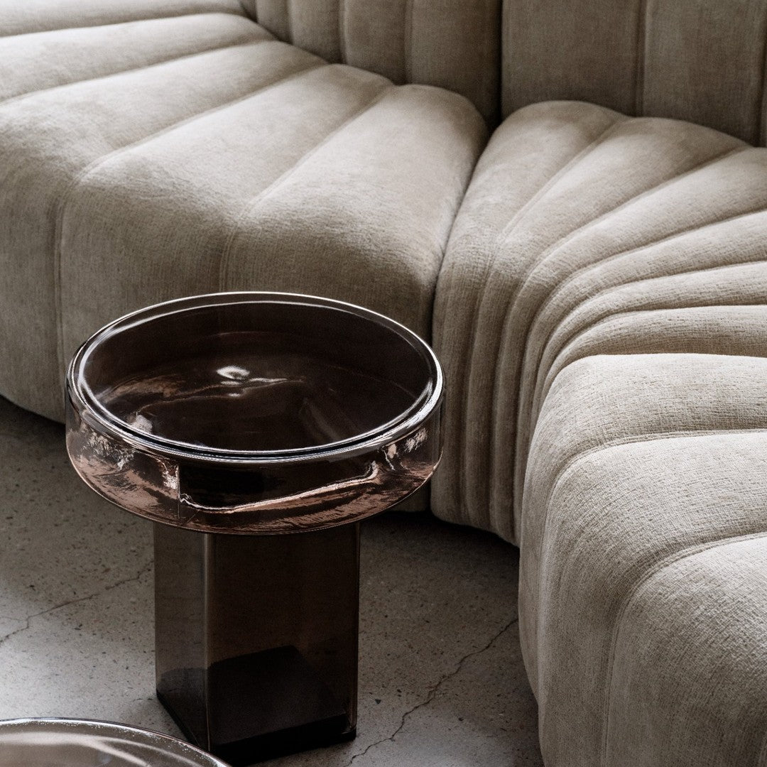 Beige tufted sofa with elegant curves and a round dark glass coffee table. Soft textures and muted tones create warmth.