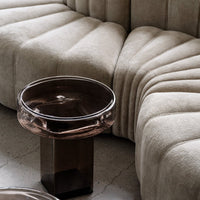 Beige tufted sofa with elegant curves and a round dark glass coffee table. Soft textures and muted tones create warmth.