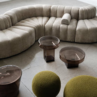 Beige curved sofa with soft texture, paired with brown glass tables and vibrant green spherical poufs on a light floor.