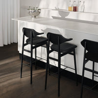 Modern black bar stools with sleek lines, set against a minimalist white countertop and warm wood floor.
