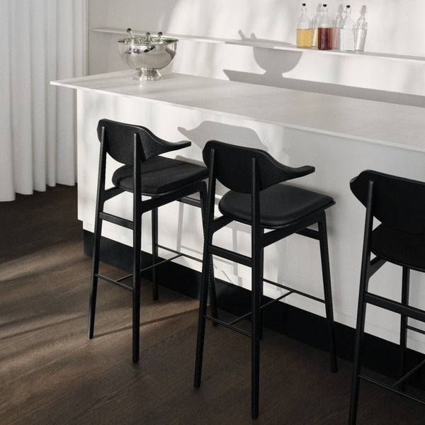 Modern black bar stools with sleek lines, set against a minimalist white countertop and warm wood floor.
