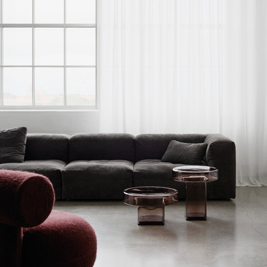 Dark gray modern couch with rich burgundy accent, complemented by translucent glass tables in warm hues.