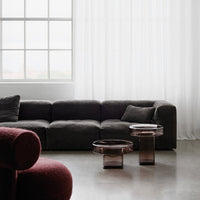 Dark gray modern couch with rich burgundy accent, complemented by translucent glass tables in warm hues.
