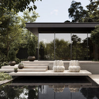 Modern patio seating in soft beige, surrounded by lush greenery and sleek black accents. Ideal for contemporary outdoor spaces.