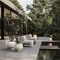 Minimalist outdoor seating and planters in white, grey, and natural wood, surrounded by lush green foliage.