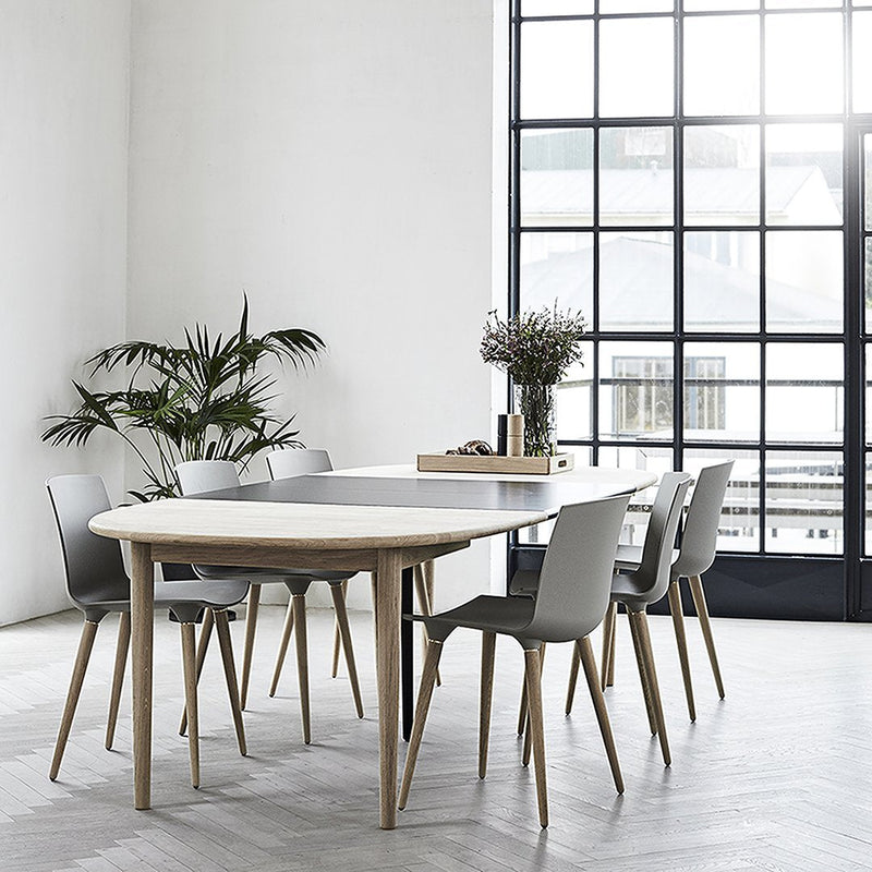 Modern round dining table with light wood finish and gray chairs, set against a bright, minimalistic backdrop.