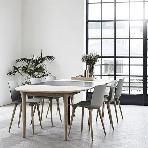 Light grey round dining table with natural wood accents, surrounded by sleek grey chairs against a bright, airy backdrop.