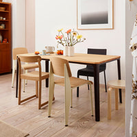 "Light wood table with mixed colored chairs in natural tones and minimal patterns, set in a bright, stylish interior."