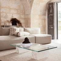 Beige sectional sofa with plaid and solid cushions, complemented by a clear glass coffee table and neutral rug.