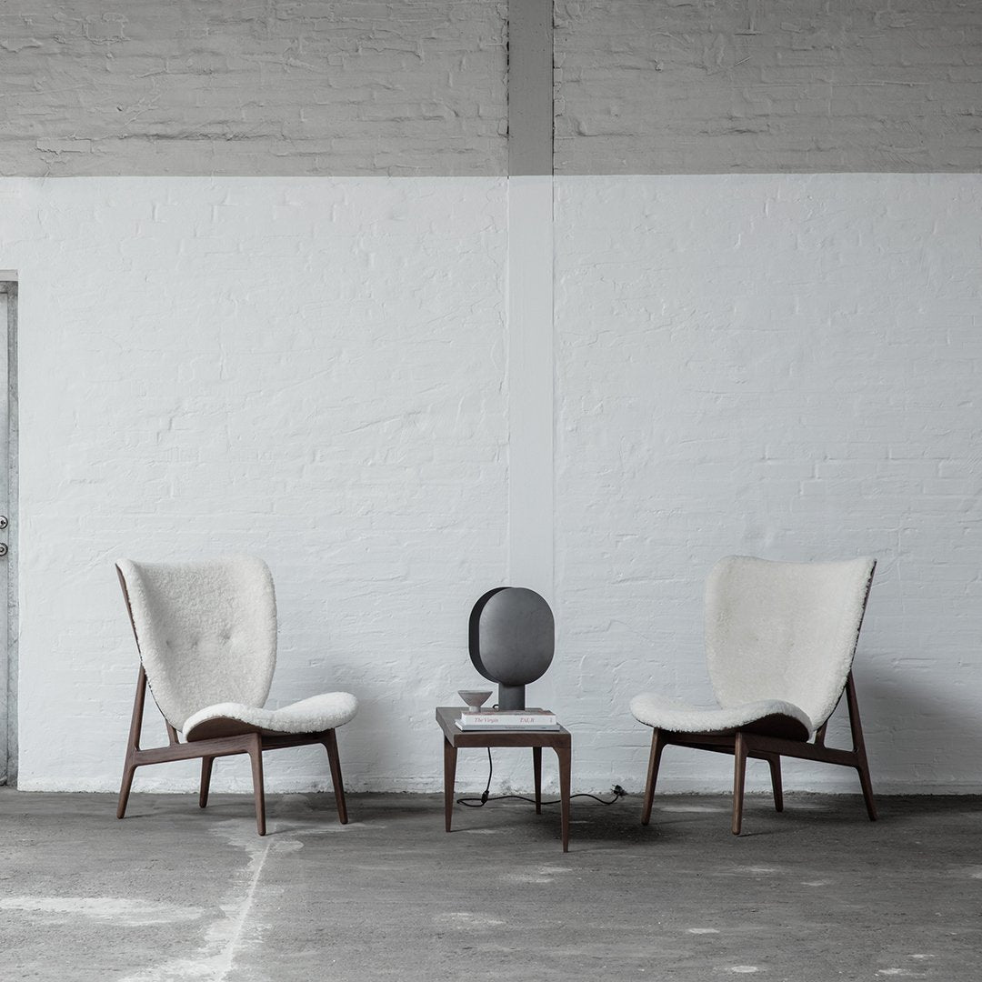 "Modern beige armchairs with wooden legs and a minimalistic gray side table in a neutral-toned space."