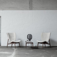 "Modern beige armchairs with wooden legs and a minimalistic gray side table in a neutral-toned space."