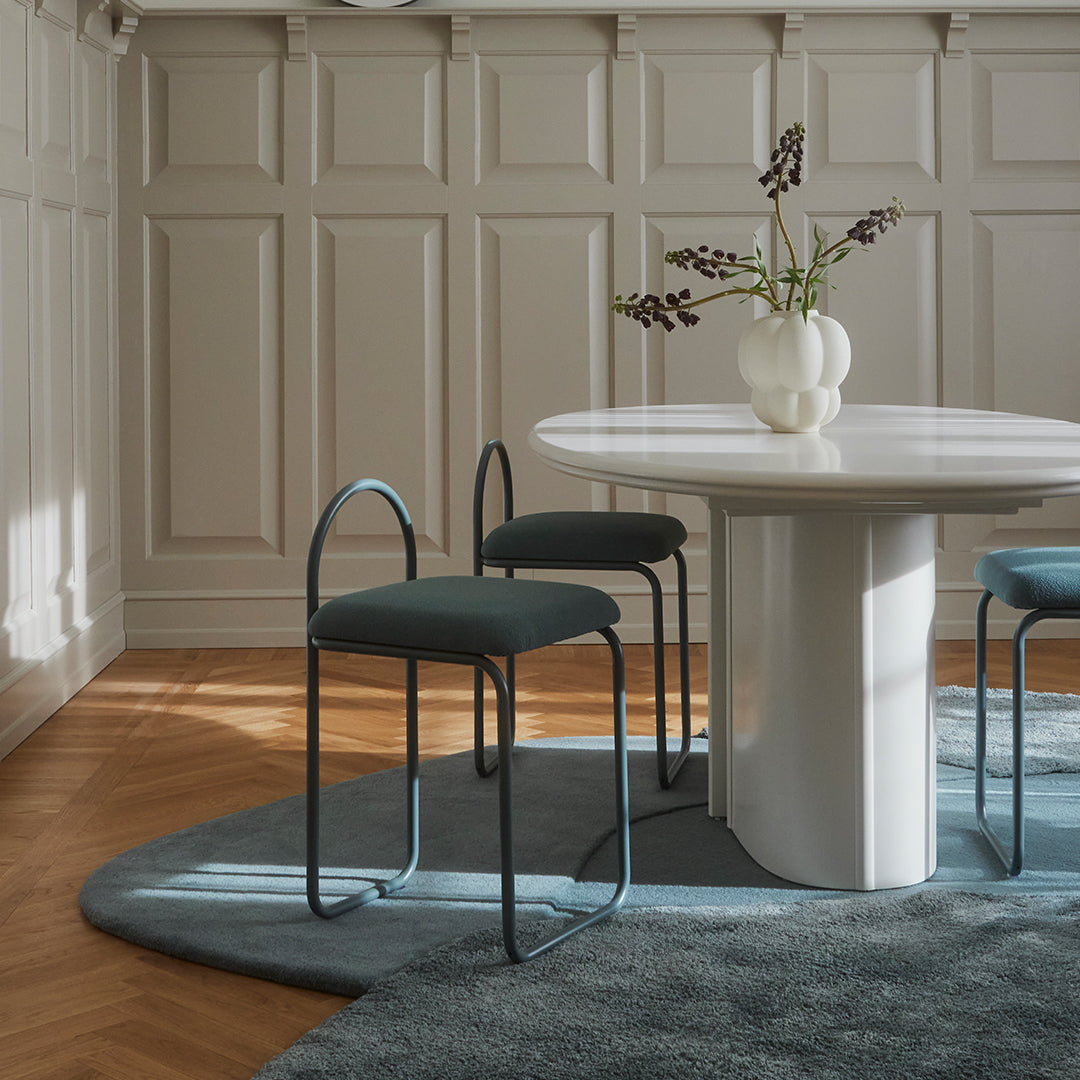 Modern dining set featuring a round white table, teal chairs, and a textured blue rug in a stylish interior.
