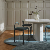 Modern dining set featuring a round white table, teal chairs, and a textured blue rug in a stylish interior.