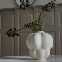 White round vase with subtle ribbed pattern, showcasing dark purple flowers against a light background.