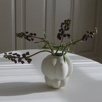 White ceramic vase with a textured pumpkin shape, showcasing beautiful purple flowers against a soft, bright background.