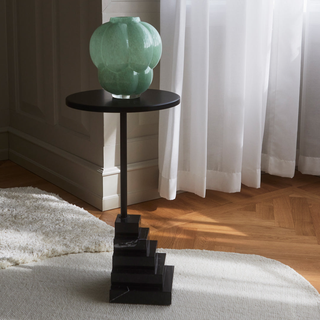 Black geometric side table with a mint green glass vase, featuring sleek lines and modern patterns.