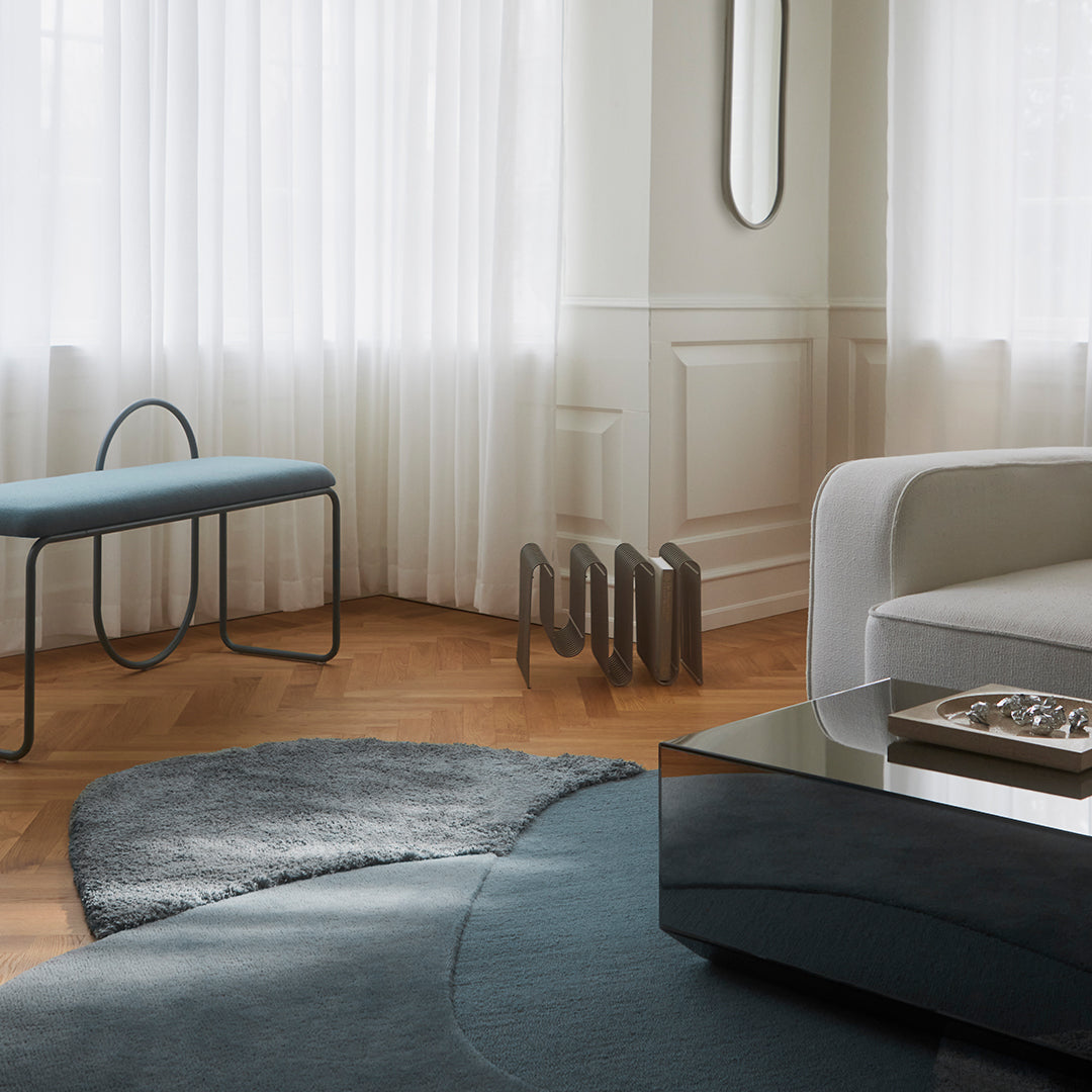 Modern living room with a gray and teal rug, sleek black coffee table, and light wood flooring. Soft, neutral curtains.