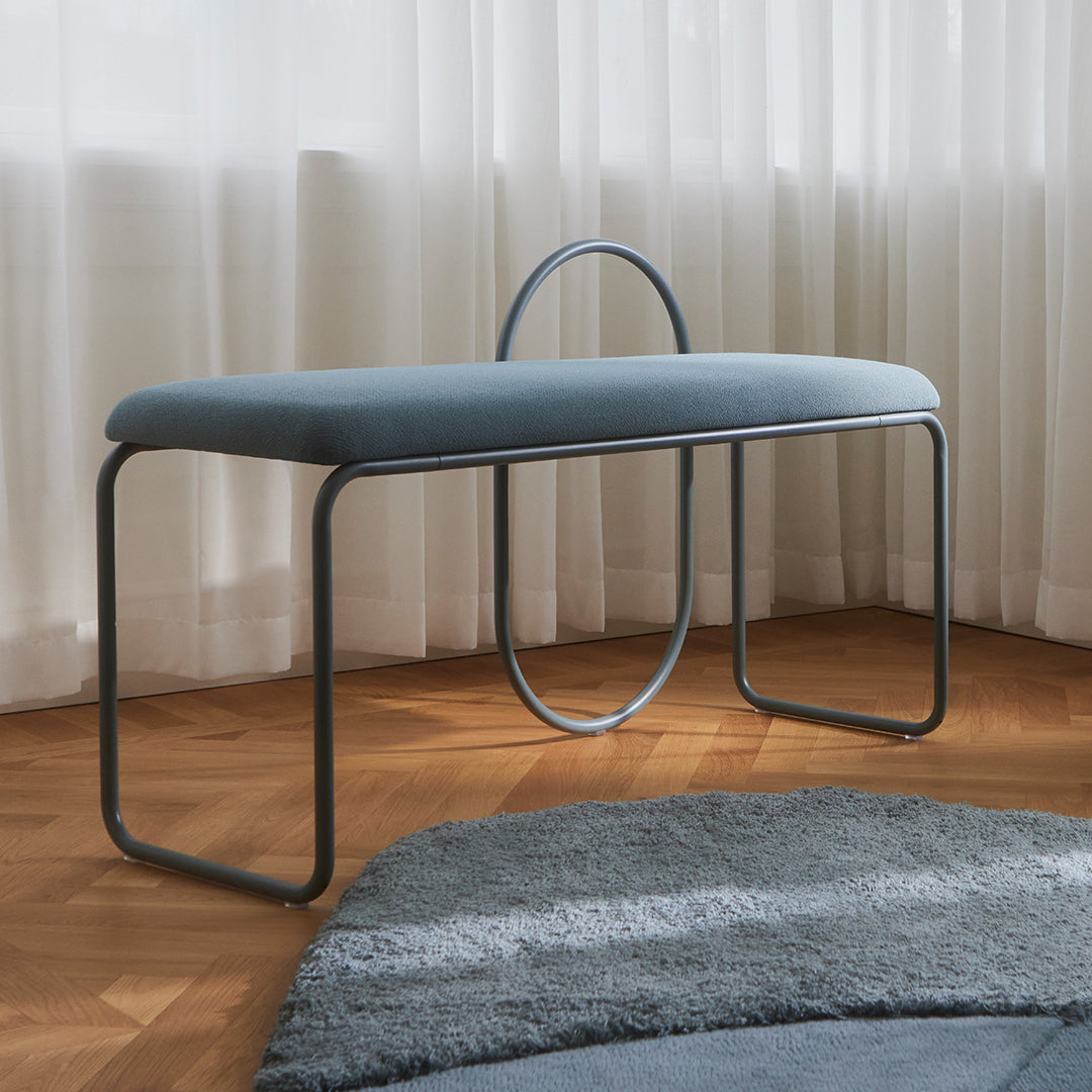 Light blue upholstered bench with minimalist design and a sleek gray metal frame, set against a soft rug.