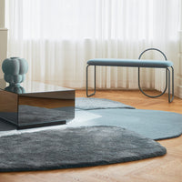 Light blue and gray area rugs with organic shapes, complemented by a sleek geometric table and soft blue accents.