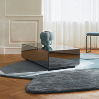 Sleek black mirrored coffee table on soft blue and gray patterned rug with a round blue vase accent.