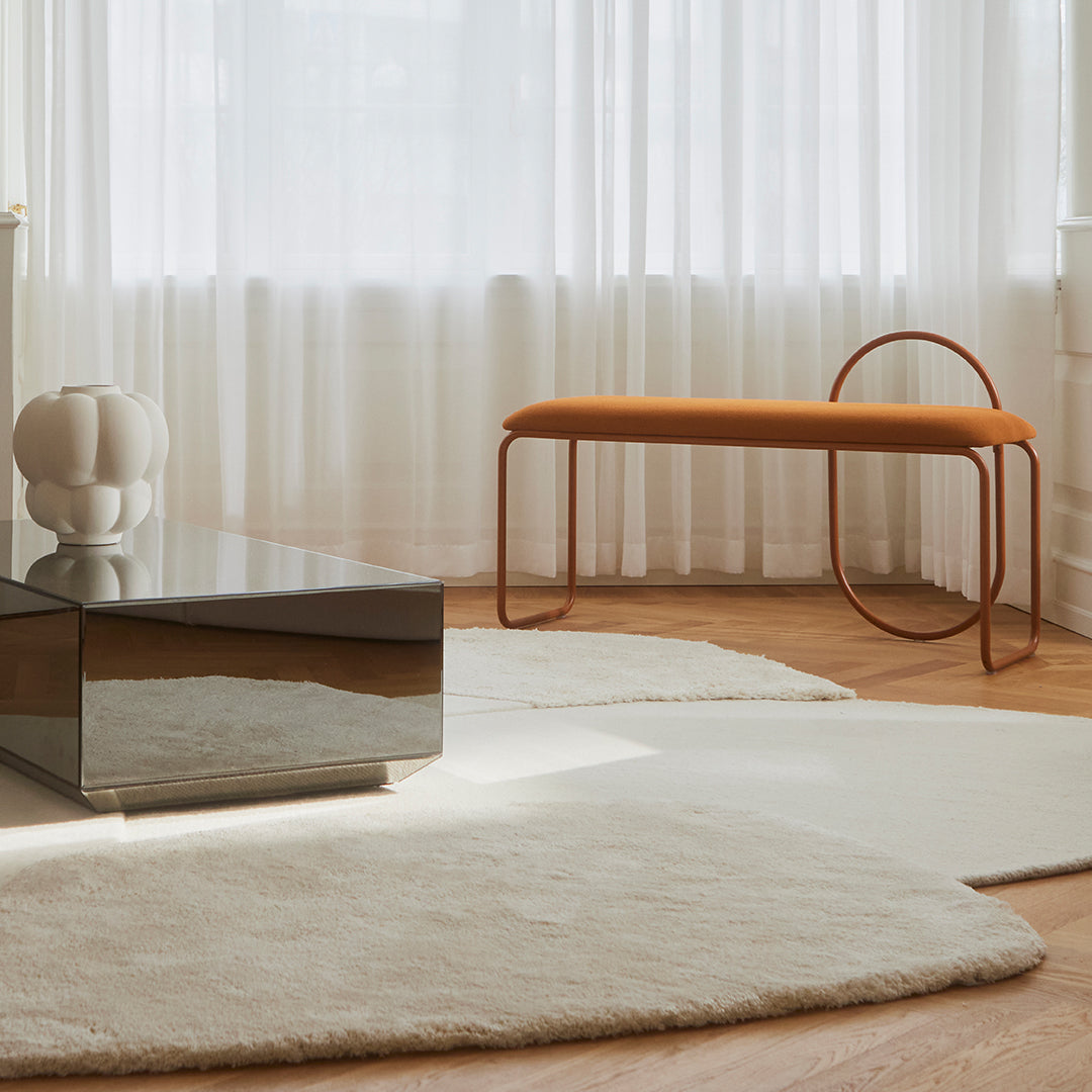 "Soft cream area rugs with a minimalist design, featuring an orange bench and reflective surfaces in a bright space."