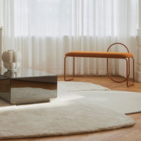 "Soft cream area rugs with a minimalist design, featuring an orange bench and reflective surfaces in a bright space."