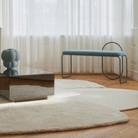 Light beige rug on hardwood floor, complemented by a soft blue bench and gray vase, with a minimalist pattern.