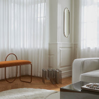 Modern living room with sheer white curtains, orange bench, and neutral-toned furniture creating a calm, inviting atmosphere.