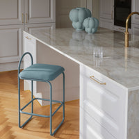 Sky blue upholstered bar stool with a sleek metal frame, set against a marbled countertop and white cabinetry.