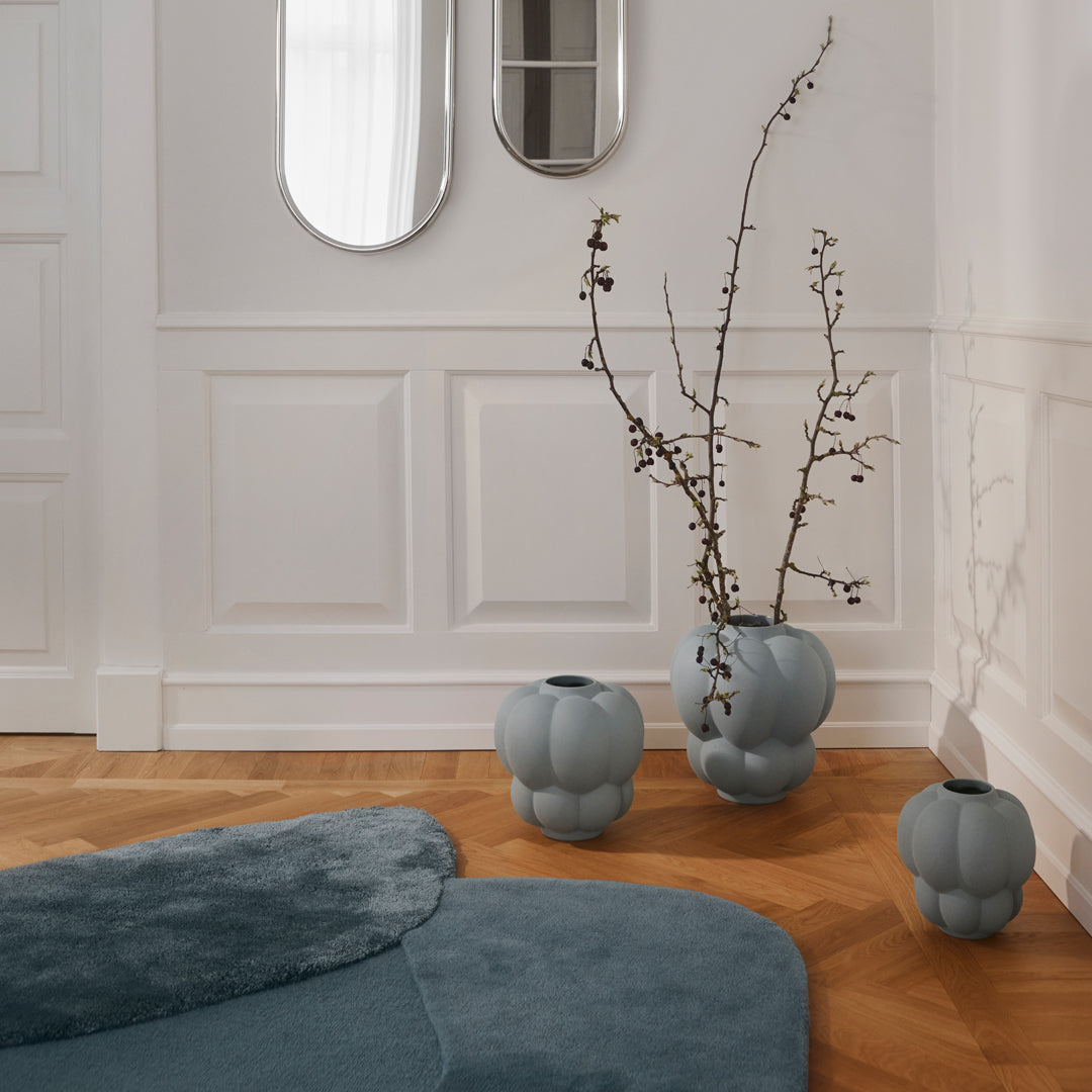 Soft blue vases with rounded shapes, complemented by a plush teal rug in a bright, airy room with wood flooring.