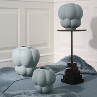 Soft blue vases with a textured, bulging pattern on a stylish black stand against a light backdrop.