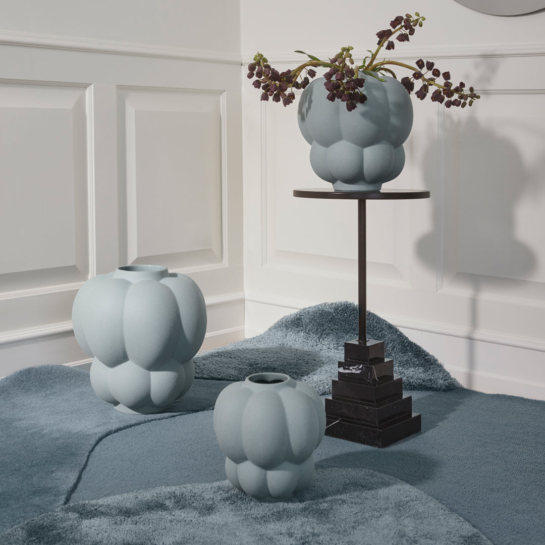 Light blue textured vases with rounded patterns displayed on a soft blue rug in a modern setting.