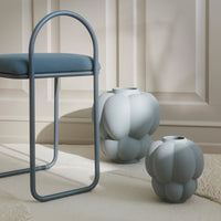 Two textured, gray vases with rounded shapes beside a blue upholstered chair against a neutral backdrop.