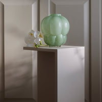 "Translucent green glass vase with a bubble pattern, placed on a light-colored pedestal against neutral backdrop."