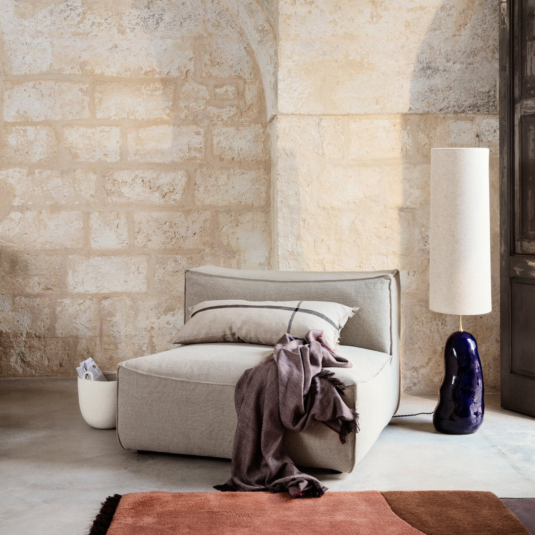 Neutral beige sofa with soft gray throw, paired with a terracotta rug and a glossy purple lamp. Modern minimalist decor.
