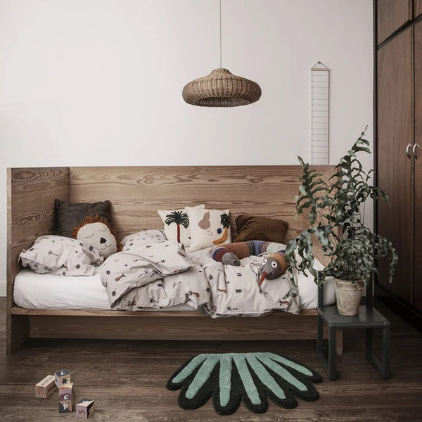 Cozy child’s bed with white bedding, animal prints, and a teal leaf-shaped rug in a warm, neutral room.