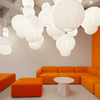 Bright orange couch and ottoman paired with white hanging lanterns in a minimalist interior design.